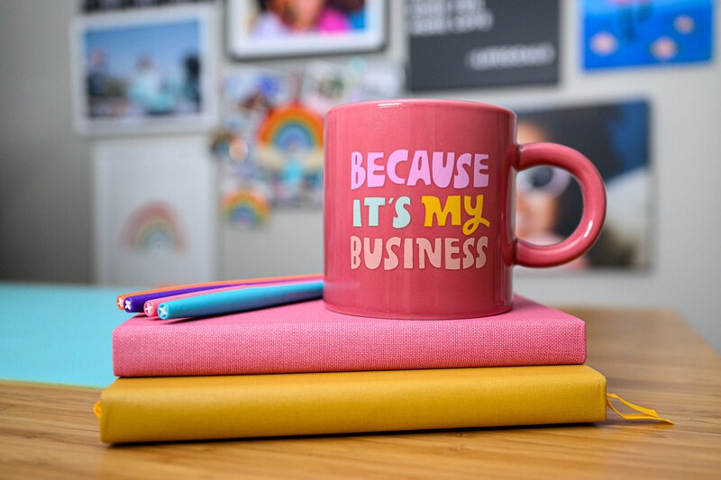 Pink mug on colorful notebooks with text “Because It’s My Business,” symbolizing Client Emails vs. Email Marketing.