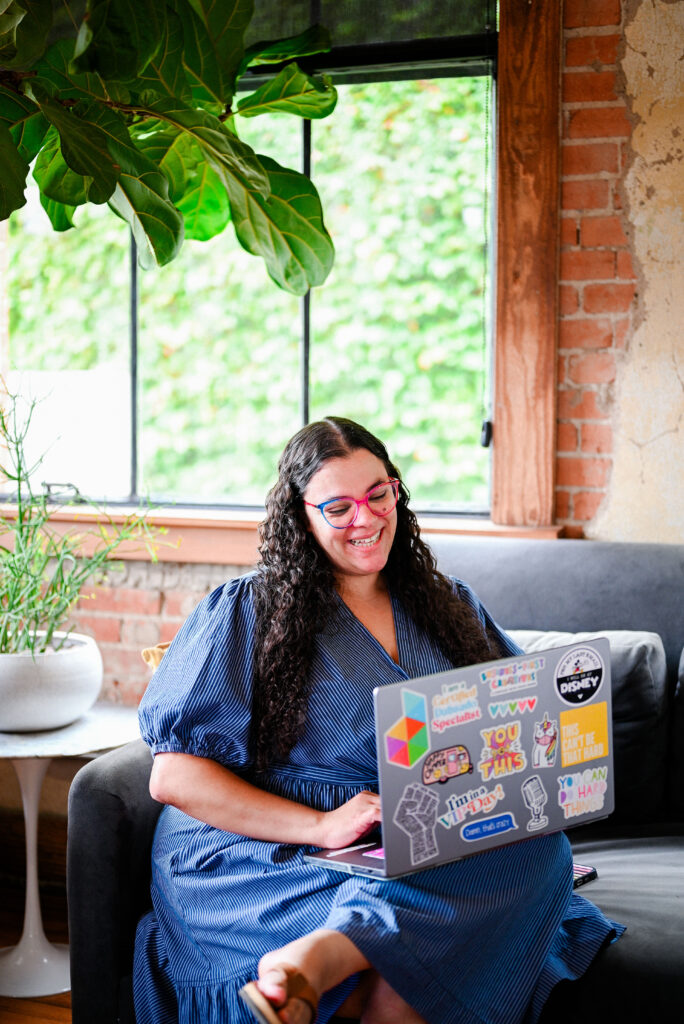 Colie James, systems expert, sits on couch on her laptop as she writes a post about how a strong email strategy can convert leads into confident bookings.